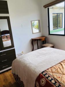 um quarto com uma cama, uma mesa e 2 janelas em Rincon Arrayán em Otavalo