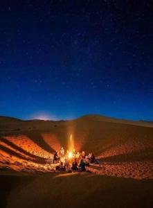 Un grupo de personas sentadas alrededor de un fuego en el desierto. en Bivouac Karim Sahara, en Zagora