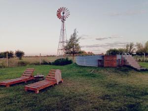 three benches sitting in a field with a windmill at Chacra CHANCAY in Mercedes