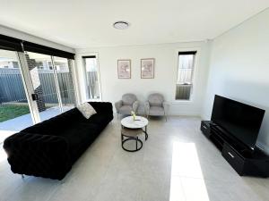 ein Wohnzimmer mit einem schwarzen Sofa und einem Flachbild-TV in der Unterkunft Brand New Luxury 4 Bedroom House in Marsden Park