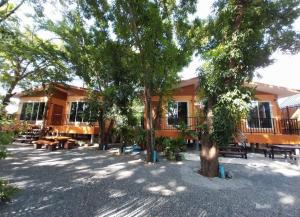 a building with tables and trees in front of it at Baansuan Tham Ma Chad Homestay in Suphan Buri