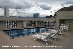 a swimming pool with white chairs on a building at Flat Sirena - São Vicente in São Vicente