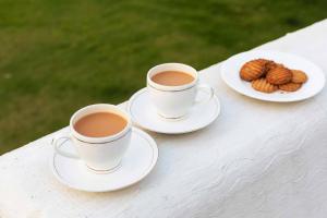two cups of coffee and a plate of cookies on a table at StayVista at Sunset Springs with Heated Swimming Pool in Nainital