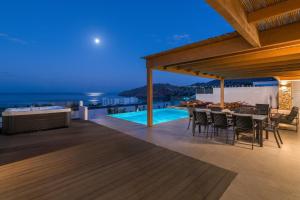 an outdoor deck with a table and chairs at night at Villa Rocabella with heated pool & jacuzzi in Lindos in vlicha