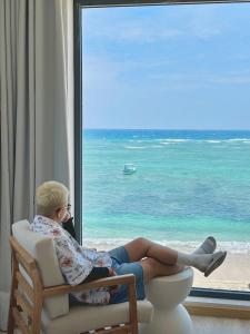 Un uomo seduto su una sedia che guarda fuori dalla finestra sulla spiaggia di La Mer Boutique House a Cù Lao Thu