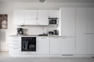 a white kitchen with white cabinets and a microwave at Vesirattaantie Apartment in Espoo