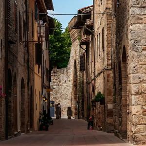 an alley with stone buildings and a person walking down the street at Locanda Il Pino in San Gimignano