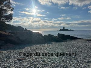 a rocky beach with a lighthouse in the distance at Superbe studio 4/5 pers dans résidence cap esterel in Agay - Saint Raphael
