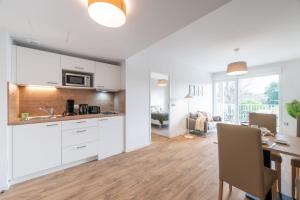 una cucina e un soggiorno con armadi bianchi e tavolo di OVELIA Saint-Saulve - Les Quatre Jardins a Saint-Saulve