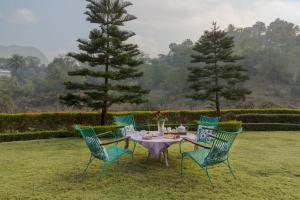 a table and four chairs with a tea set on the grass at SaffronStays Sylvan Farms - 3BR eco-luxury villa with birdwatching, trekking and organic farming in Mount Abu in Delmāra