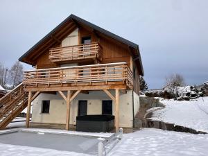 a house with a balcony on top in the snow at Chalet PLUME D'EAU - jacuzzi, piscine et pétanque in Gerbépal