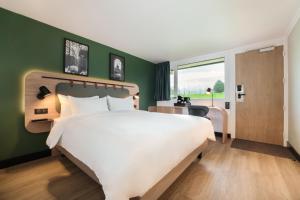Un dormitorio con una gran cama blanca y una pared verde. en Campanile NATURE - Thionville Yutz, en Basse-Yutz