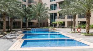 a swimming pool with palm trees in front of a building at Luxury 2-bed Condo Full Burj Khalifa Lights View! in Dubai