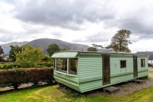 a green trailer parked in a field with mountains in the background at Osprey Caravan in Onich