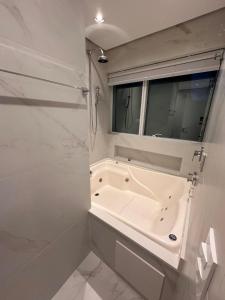 a white bathroom with a tub and a window at Loft Duplex com Hidromassagem in Florianópolis +7 photos