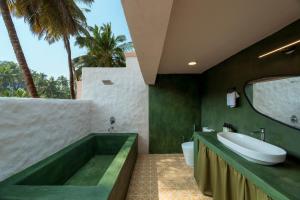 a bathroom with a tub and a sink and palm trees at ALTR NATIV Morjim, Goa in Morjim