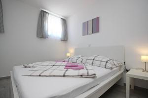 a white bedroom with a white bed with pink pillows at House Lavanda - Kricin, underground level apartment in Baška