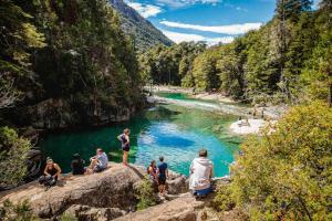a group of people sitting on rocks near a river at Cabañas Terraza Sur in El Bolsón