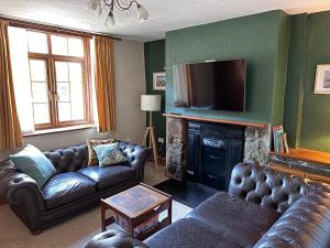 a living room with leather couches and a television at Bwythyn Ebrill, April Cottage in Betws-y-coed