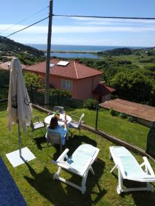 Eine Frau, die an einem Tisch mit Stühlen und einem Regenschirm sitzt. in der Unterkunft Doniños Paraíso in Ferrol