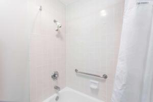 a bathroom with a shower with a white tub at Ramada by Wyndham Oceanside in Oceanside