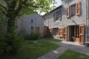 - un bâtiment en pierre avec des portes en bois et un arbre dans l'établissement Gîte Gîtes de France 6/7 personnes au Fau de Peyre, à Fau-de-Peyre
