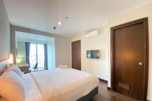 a bedroom with a white bed and a wooden door at Spacious 2BR Apartment at El Royale near BIP By Travelio in Bandung