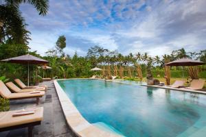a large swimming pool with chairs and umbrellas at Om Ham Retreat and Resort in Ubud