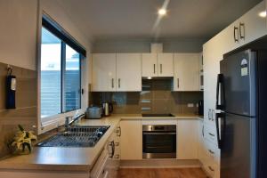 a kitchen with white cabinets and a stainless steel refrigerator at Paperbark Cottage in Callala Bay