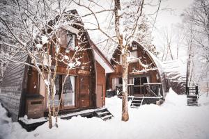 a house covered in snow next to a tree at The Cabin in Hakuba