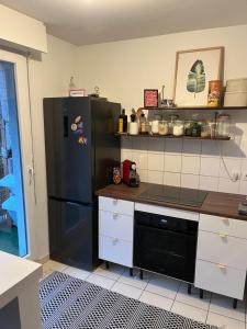 a kitchen with a black refrigerator and white cabinets at Appartement Paisible au Vert in Saint-Ouen