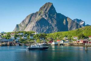 a boat in the water in front of a mountain at Madelhea Cabin- Seaview Lodge in Reine +16 photos
