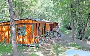 a woman standing in front of a cabin in the woods at Bungalow confortable à Escaro avec piscine partagée in Escaro