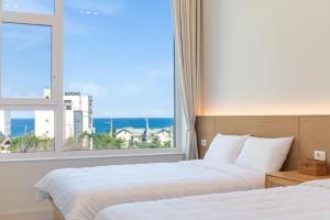 two beds in a hotel room with a large window at Gangneung Atopool Villa in Gangneung