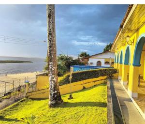a yellow building with a palm tree next to a beach at Casa na praia do bispo pa in Mosqueiro
