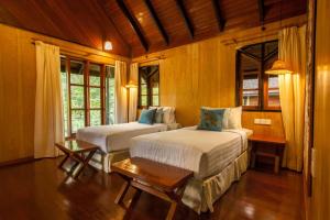 a bedroom with two beds and a table and windows at Sepilok Nature Lodge - Formerly known as Sepilok Nature Resort in Sandakan