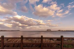 a fence next to a body of water with clouds at Jeju Sol Pension Jeju Sunrise from the Room in Chung-dong