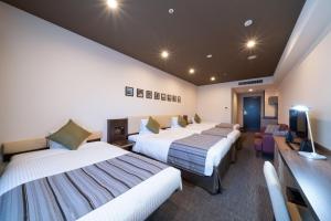 a hotel room with three beds and a television at HOTEL MYSTAYS PREMIER Kanazawa in Kanazawa