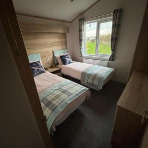 two beds in a small room with a window at The Retreat 8 Lodge - Hot tub, WiFi, pet friendly, bath - Golden Palm Resort - Meadow Lakes Caravan & Lodge Hire in Chapel Saint Leonards