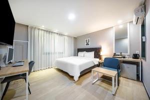 慶州市にあるBrown Dot Hotel Angangの白いベッドとデスクが備わるホテルルームです。