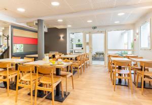 une salle à manger avec des tables et des chaises en bois dans l'établissement B&B HOTEL Nantes Aéroport, à Bouguenais
