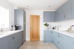 a kitchen with blue cabinets and a wooden door at Beach house for 10 with hot tub & garden in West Wittering