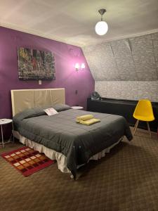 Un dormitorio con una cama con paredes moradas y una silla amarilla. en Hotel Toesca, cercano a Movistar Arena, en Santiago