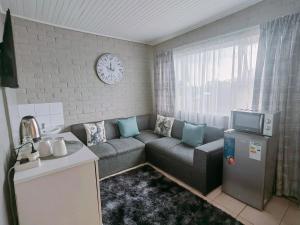Una sala de estar con un sofá y un reloj en la pared. en Zhantique Guest House 2- Unit 9, en Boksburg