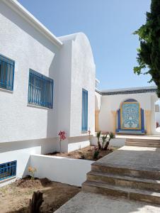 a white building with blue windows and stairs at Villa Azur Haouaria in Sidi Amor