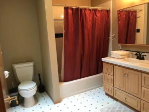 a bathroom with a toilet and a red shower curtain at Beautiful Lake Lodge with Huge Private Dock in Spanaway +42 photos
