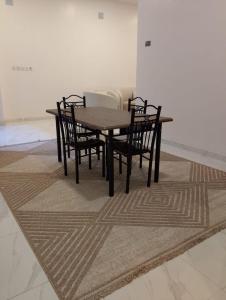 a wooden table and chairs in a room with a rug at الوعل للشقق الفندقية بالارطاوية in Al Arţāwīyah