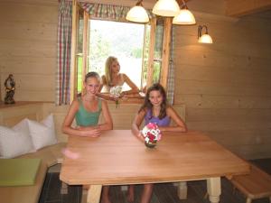 tres chicas sentadas en una mesa en una cabaña de madera en Ferienhütte Wolfgangsee, en St. Wolfgang
