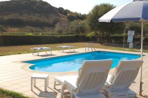 a swimming pool with two chairs and an umbrella at Villa EMPATJA in Tertenìa