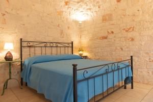 a bedroom with a bed with blue sheets and a stone wall at Trulli Mirabilis in Cisternino